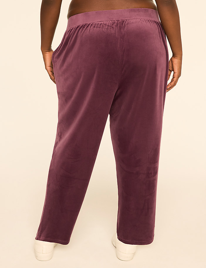 A person wearing plum-colored velvet pants stands against a plain, light-colored background.