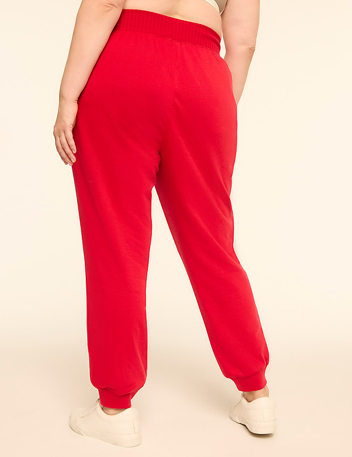 A person wearing red sweatpants and white sneakers stands against a plain, light-colored background.