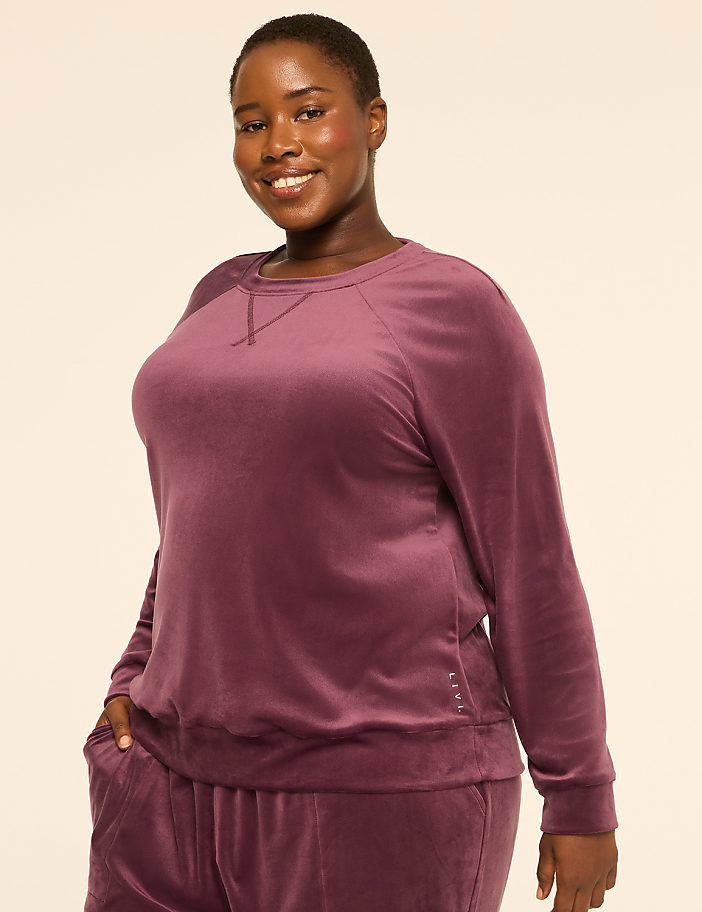 A smiling woman in a purple velvet sweatshirt and pants stands against a plain, light-colored background.