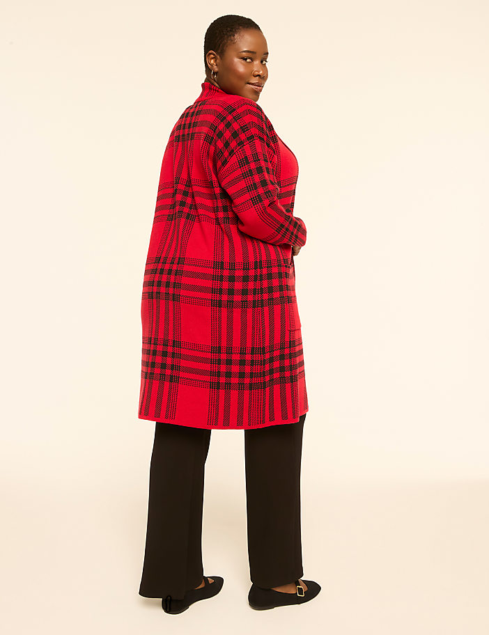 A woman in a red plaid cardigan and black pants stands against a plain, light-colored background.