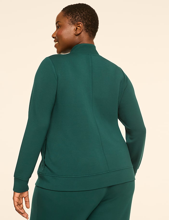 A woman in a teal jacket and pants stands against a plain, light-colored background.