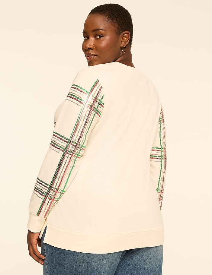 A woman in a cream-colored sweatshirt with plaid sleeves stands against a plain, light-colored background.
