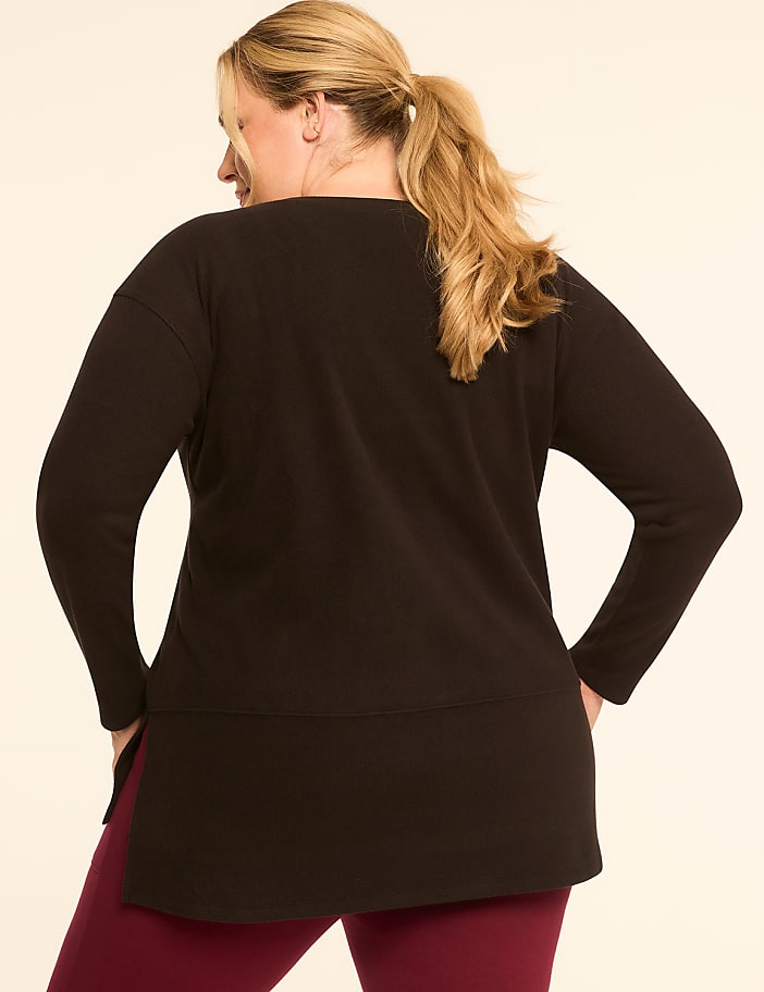 A woman in a black tunic and maroon leggings stands against a plain, light-colored background.