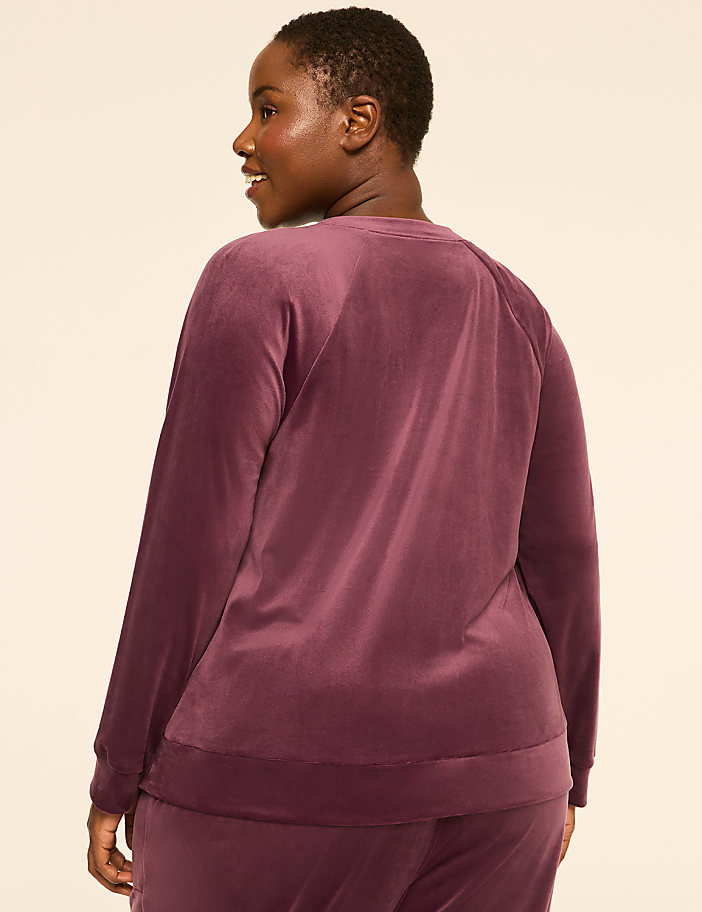 A woman in a plum-colored velour sweatshirt and pants stands against a plain, light-colored background.