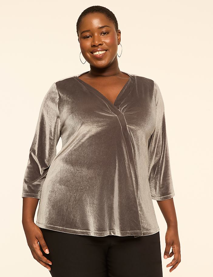 A smiling woman in a silver velvet top stands against a plain, light-colored background.