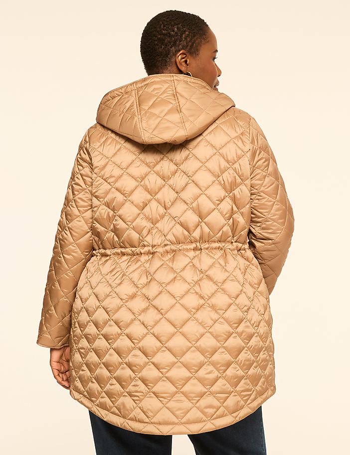A woman in a tan quilted hooded jacket with a cinched waist stands against a plain beige background.