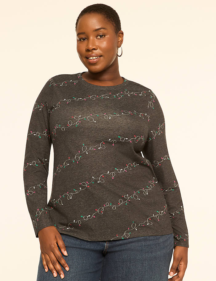 A woman in a dark gray long-sleeved shirt with a string light pattern stands against a plain, light-colored background.