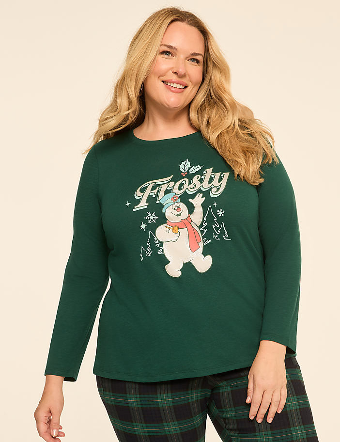 A smiling woman in a green long-sleeved shirt with a Frosty the Snowman graphic stands against a plain, light-colored background.