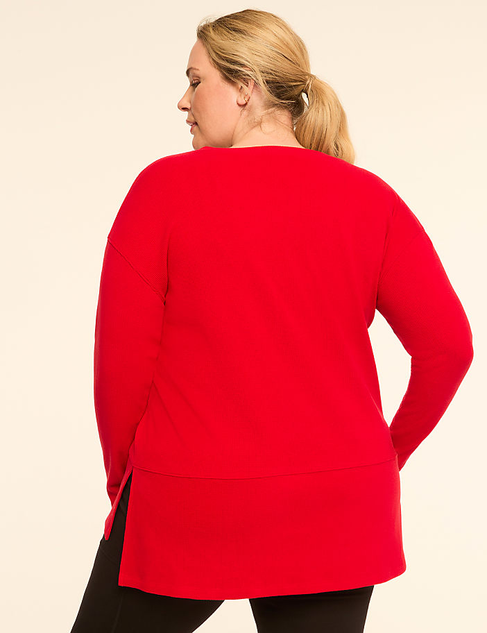A woman in a red sweater and black leggings stands against a plain, light-colored background.