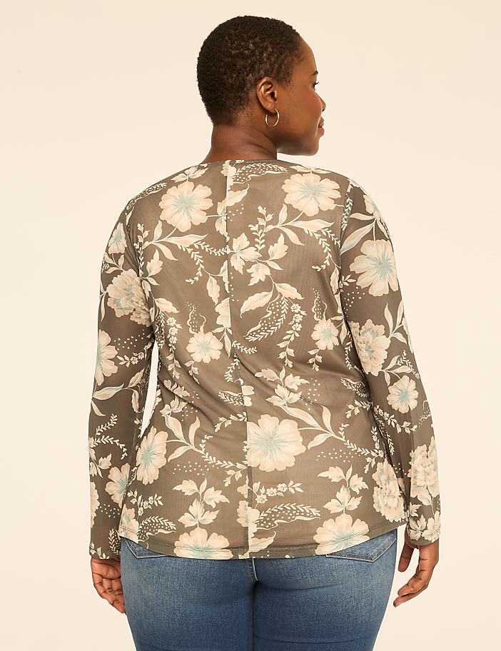 A woman in a floral top and jeans stands against a plain, light-colored background.