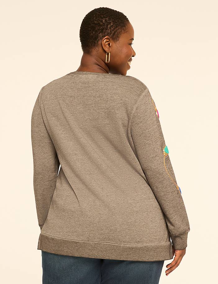 A woman in a gray sweatshirt with colorful string lights on the sleeve stands against a plain, light-colored background.