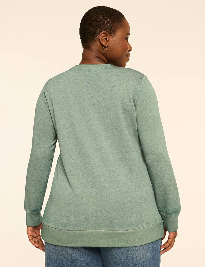 A woman in a green sweatshirt stands against a plain, light-colored background.