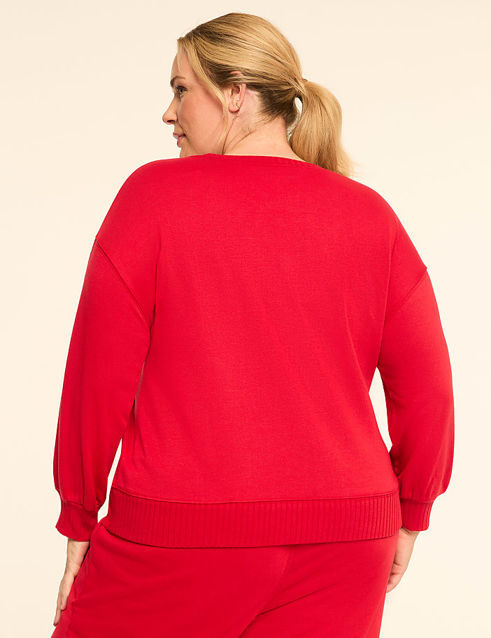 A woman in a red sweatshirt and pants stands against a plain, light-colored background.