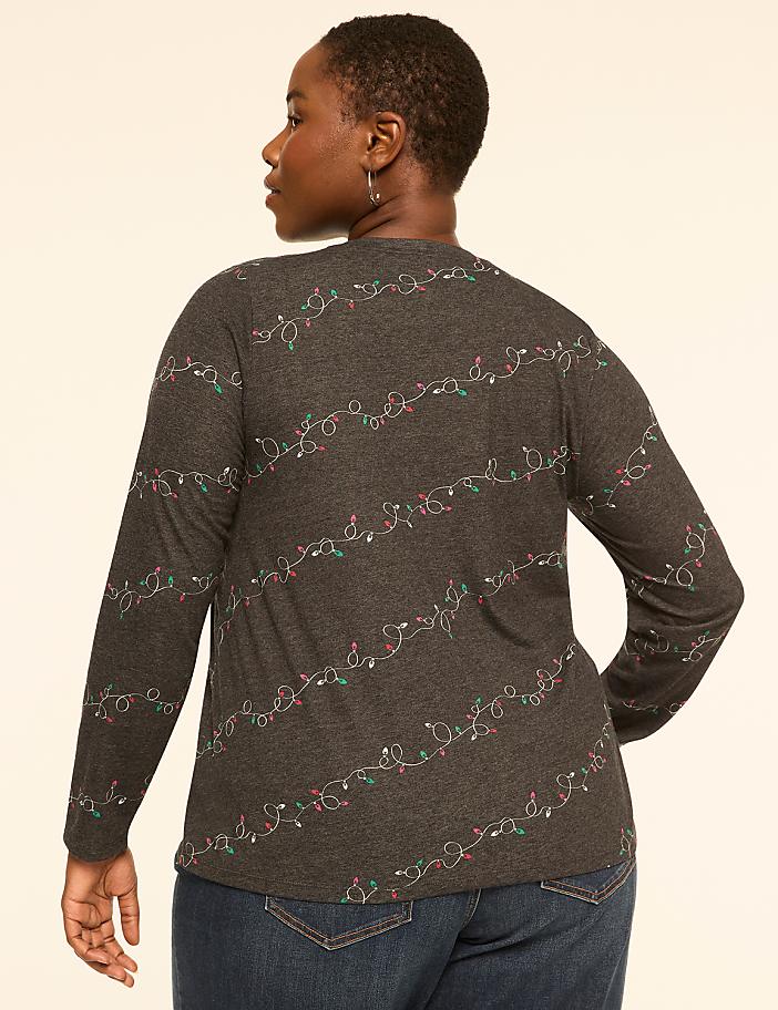 A woman in a dark grey long-sleeved shirt with a string light pattern stands against a plain, light-colored background.