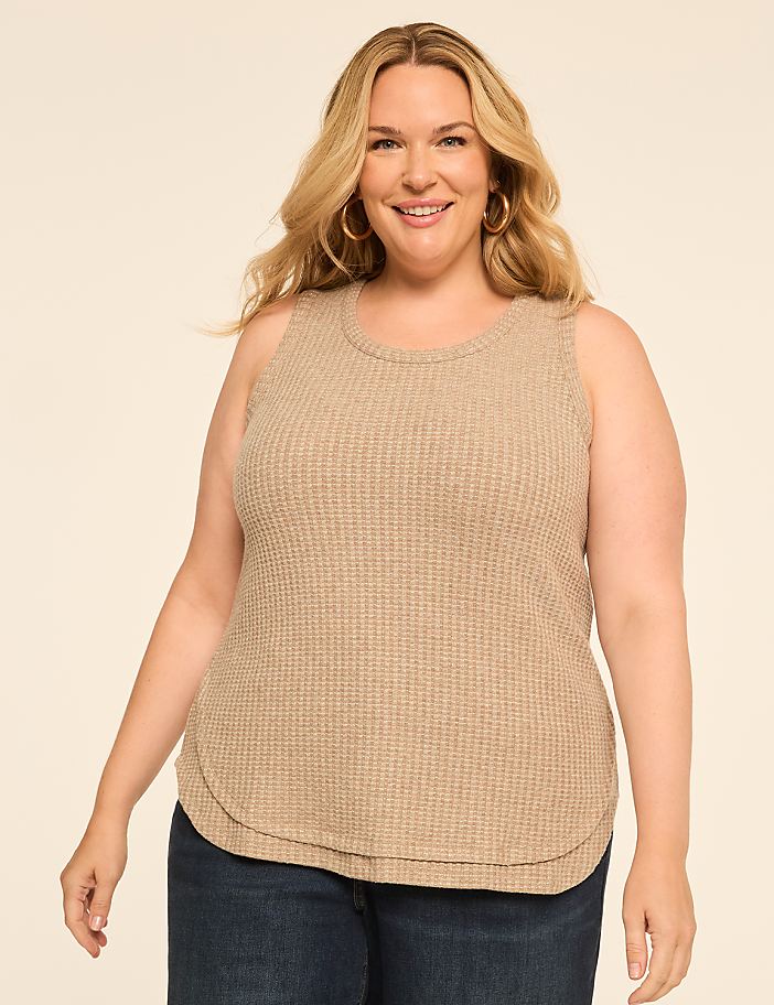 A smiling woman with blonde hair and hoop earrings poses in a tan waffle-knit tank top and blue jeans against a plain, light-colored background.