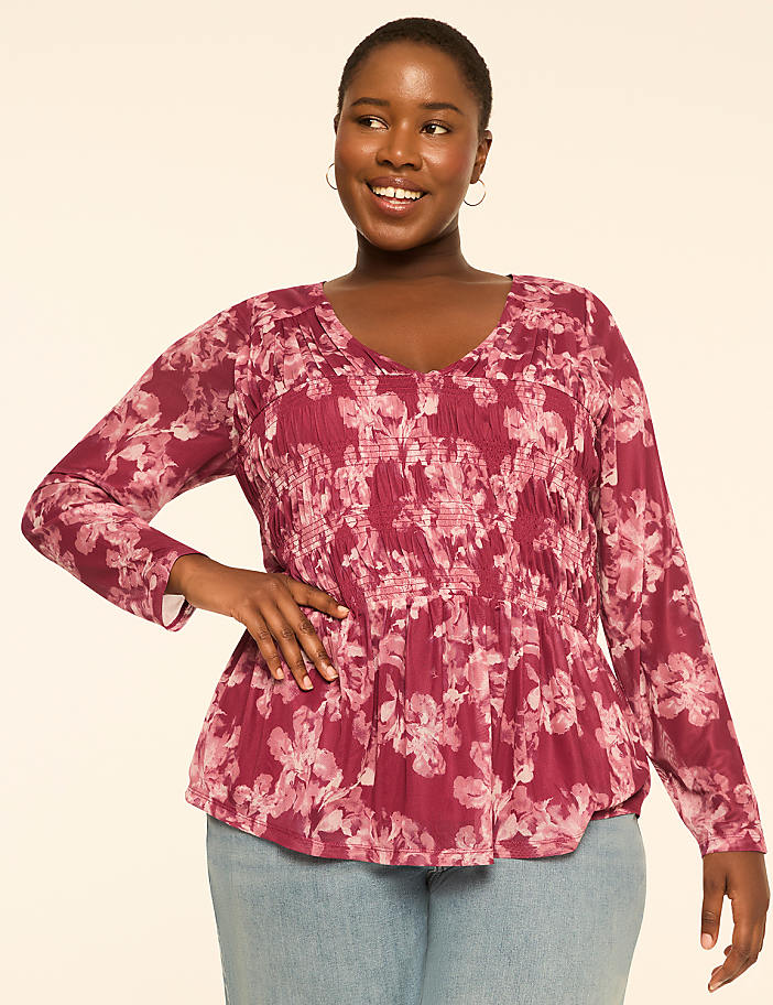 A smiling woman in a floral peplum top stands against a plain, light-colored background.