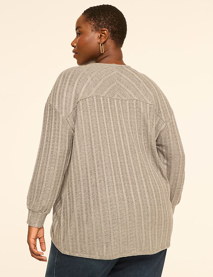 A woman in a grey textured sweater stands against a plain cream background.
