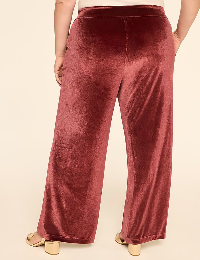 A person wearing rust-colored velvet palazzo pants stands against a plain, light-colored background.