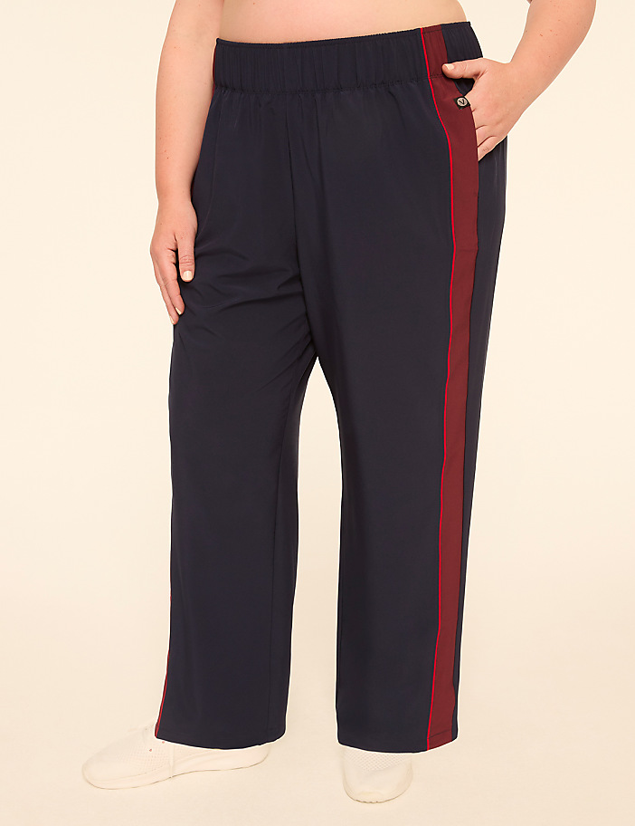 A person wearing navy blue track pants with a maroon stripe stands against a plain, light-colored background.
