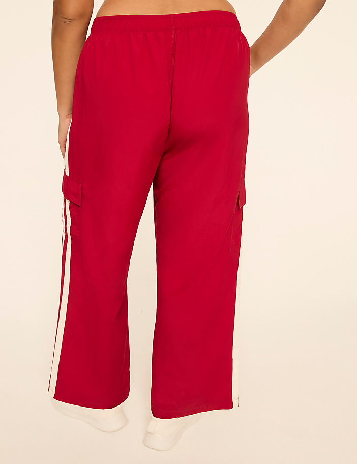 A person wearing red cargo pants with white stripes stands against a plain, light-colored background.