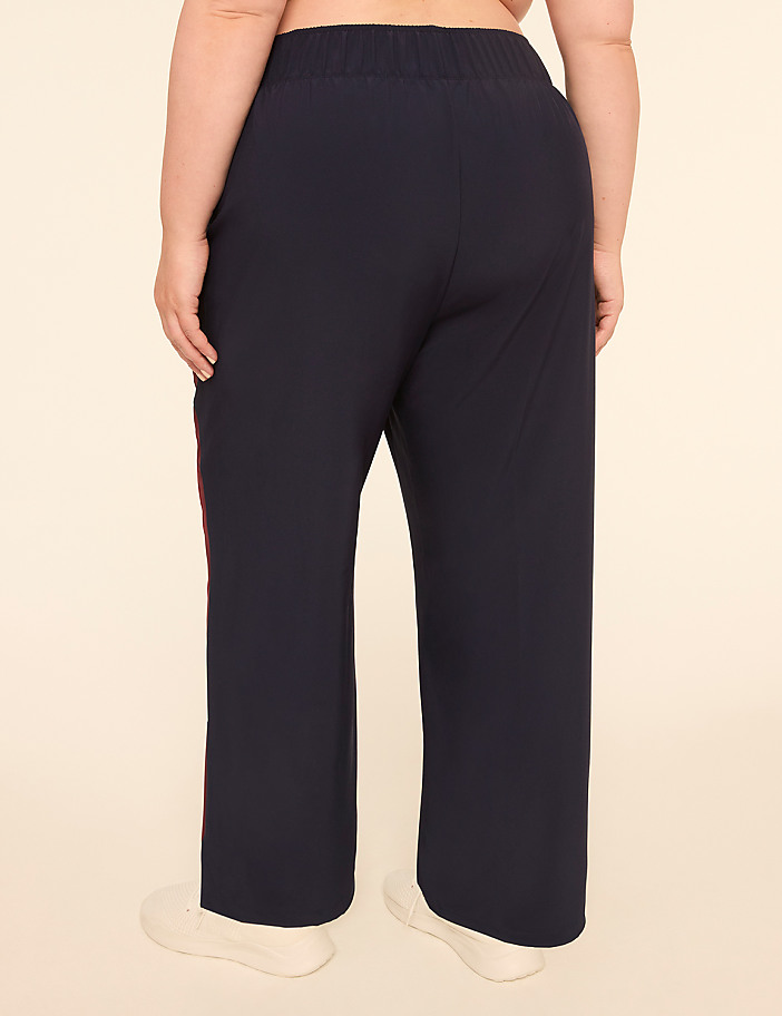 A person wearing dark blue pants with a red stripe down the side stands against a plain, light-colored background.