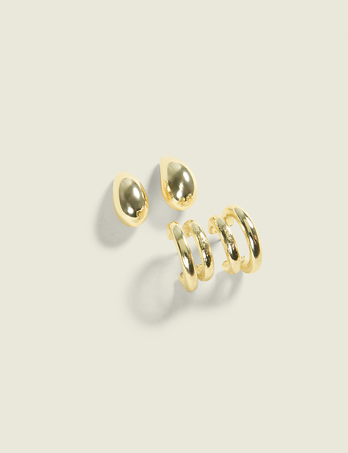Two gold teardrop earrings and three gold hoop earrings rest on a pale, textured surface.