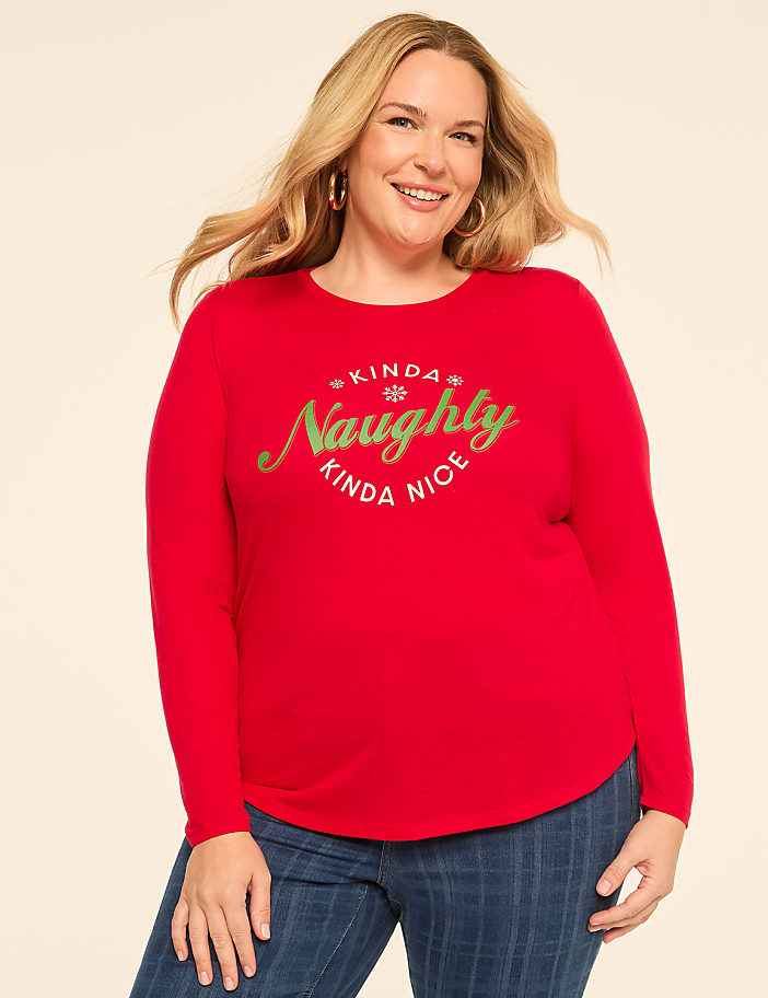 A smiling woman in a red "Kinda Naughty Kinda Nice" sweater stands against a plain, light-colored background.