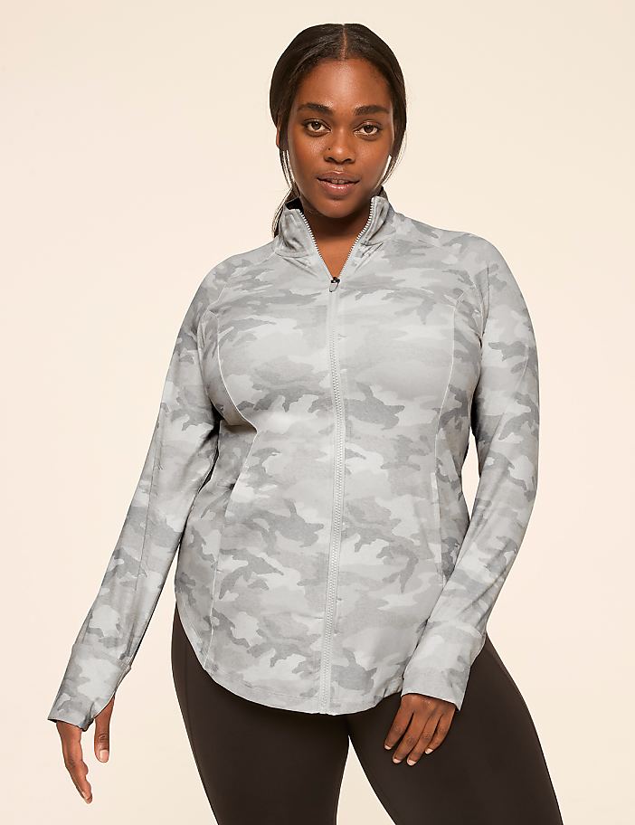 A woman in a light-colored camouflage jacket and black leggings stands against a plain, light background.