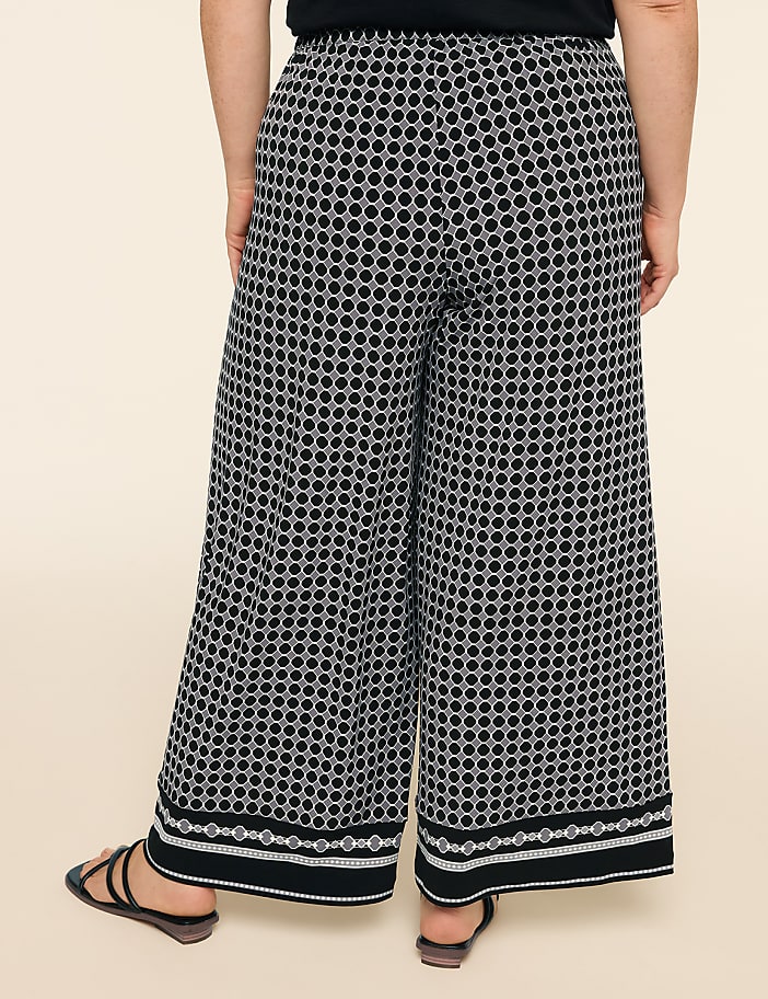 A person stands in wide-leg patterned pants with a plain background.