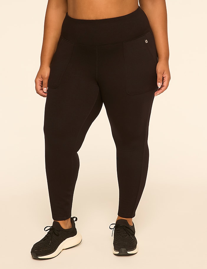 A woman in black leggings and sneakers stands against a plain, light-colored background.