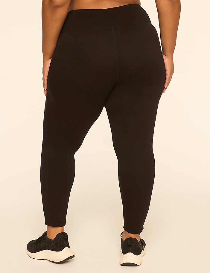 A person wearing black leggings and sneakers stands against a plain, light-colored background.