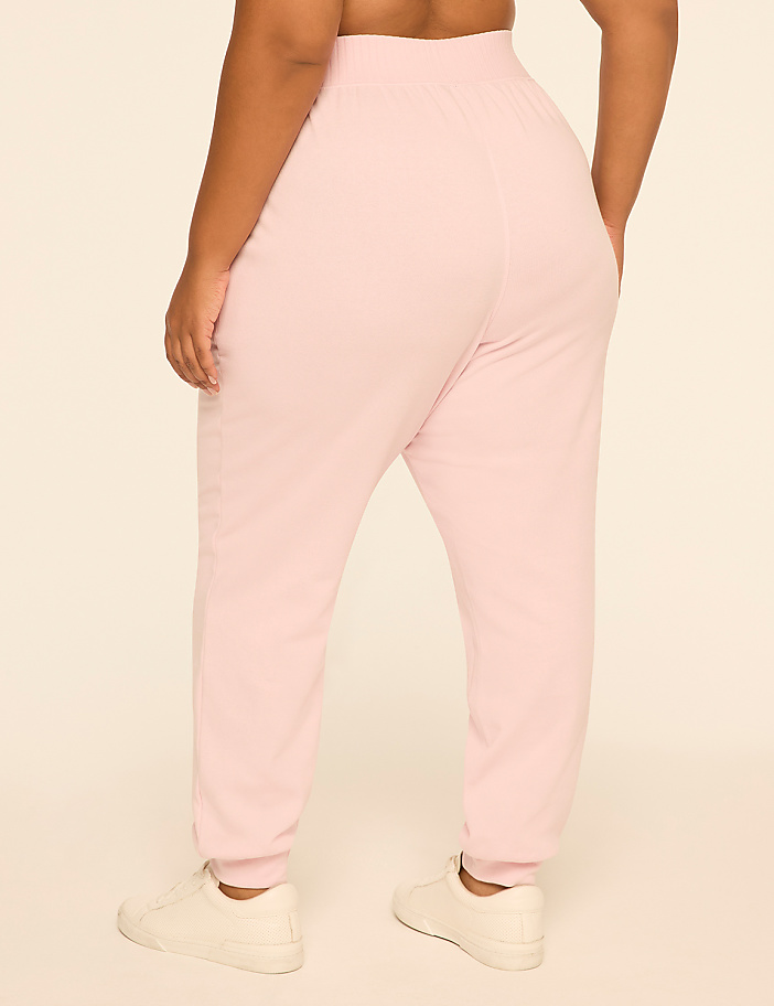 A person wearing light pink sweatpants and white sneakers stands against a plain, light-colored background.
