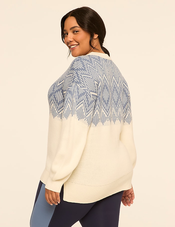A woman in a cream and blue patterned sweater and leggings stands against a plain, light-colored background.