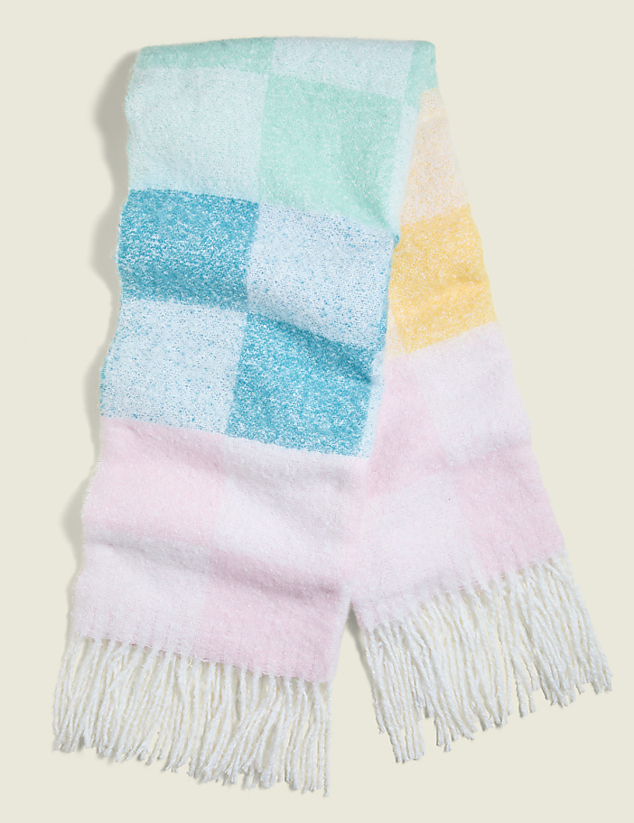 A pastel checkered blanket with fringed ends lies on a plain, light-colored background.