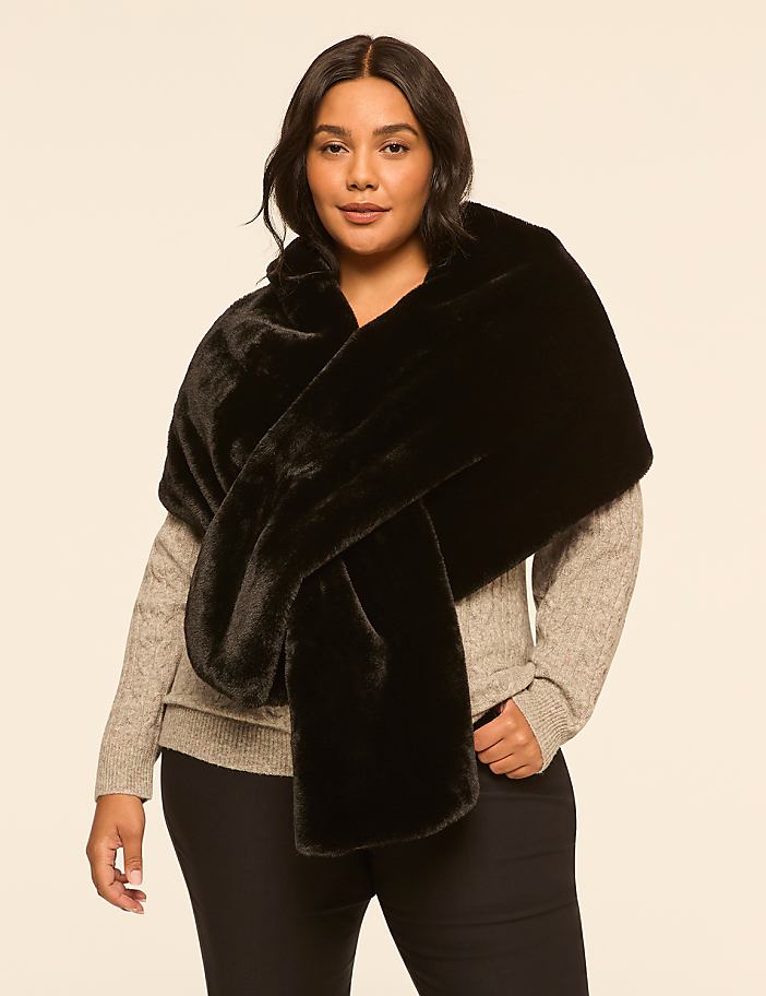 A woman in a gray sweater and black pants models a plush black faux fur stole against a plain, light-colored background.