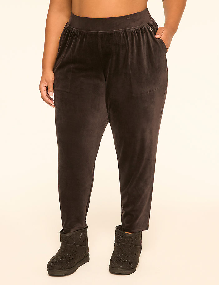 A person wearing brown velvet pants and black Ugg boots stands against a plain cream background.