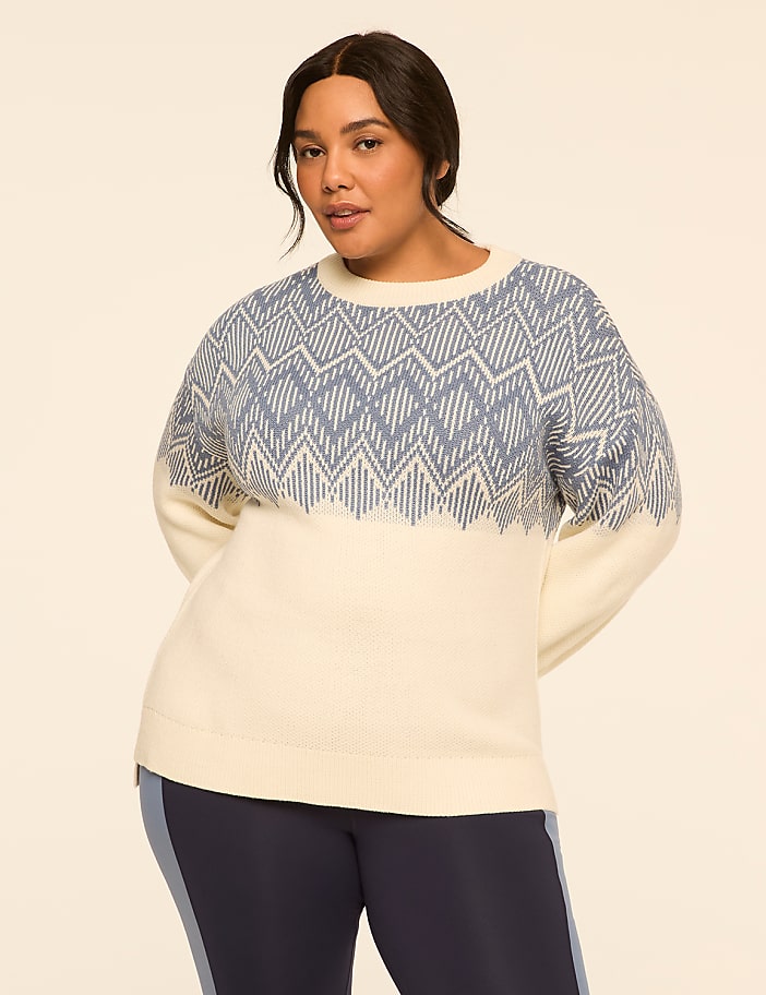 A woman in a cream and blue patterned sweater stands against a plain, light-colored background.