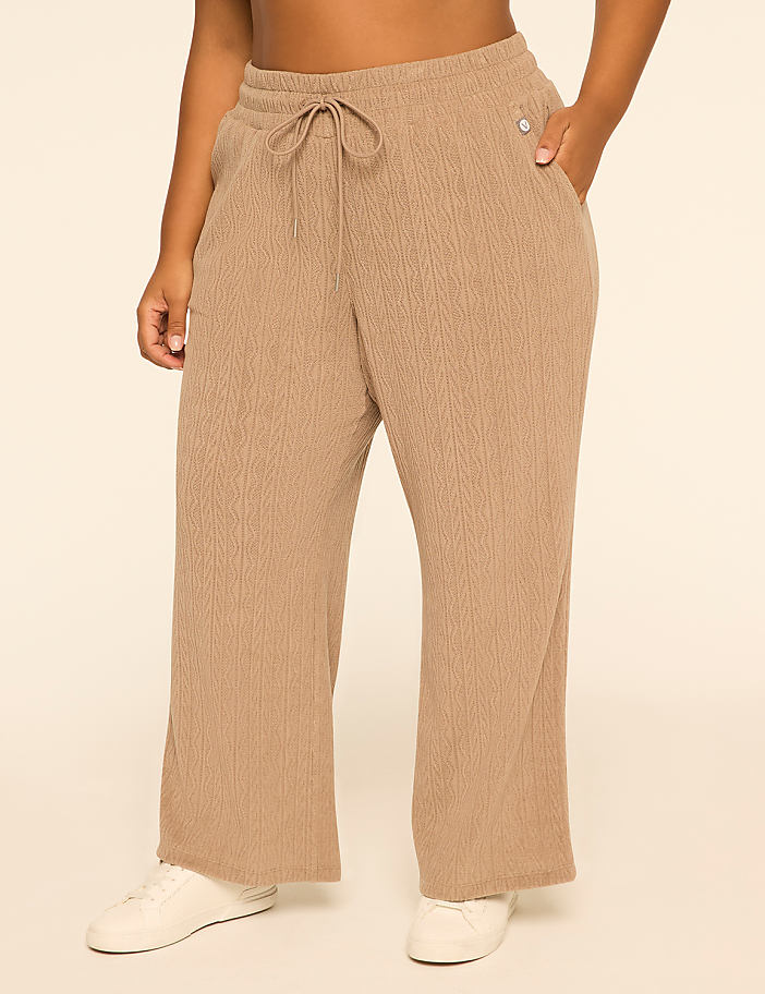 A person wearing loose-fitting, textured tan pants with white sneakers stands against a plain, light-colored background.