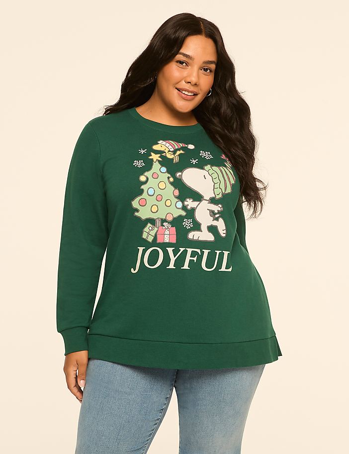 A woman in a green Christmas sweatshirt with Snoopy and Woodstock stands against a plain, light-colored background.