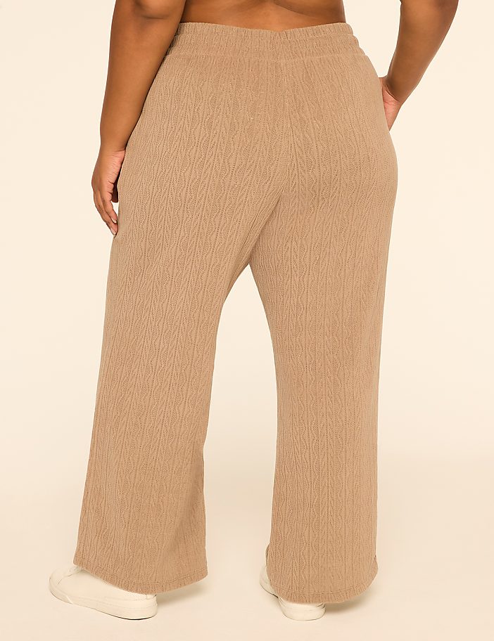 A person wearing tan, wide-leg, textured pants stands against a plain, light-colored background.
