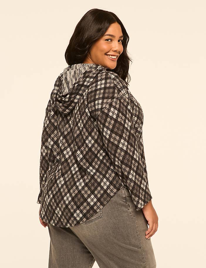 A woman in a plaid hoodie and jeans smiles over her shoulder against a plain, light-colored background.