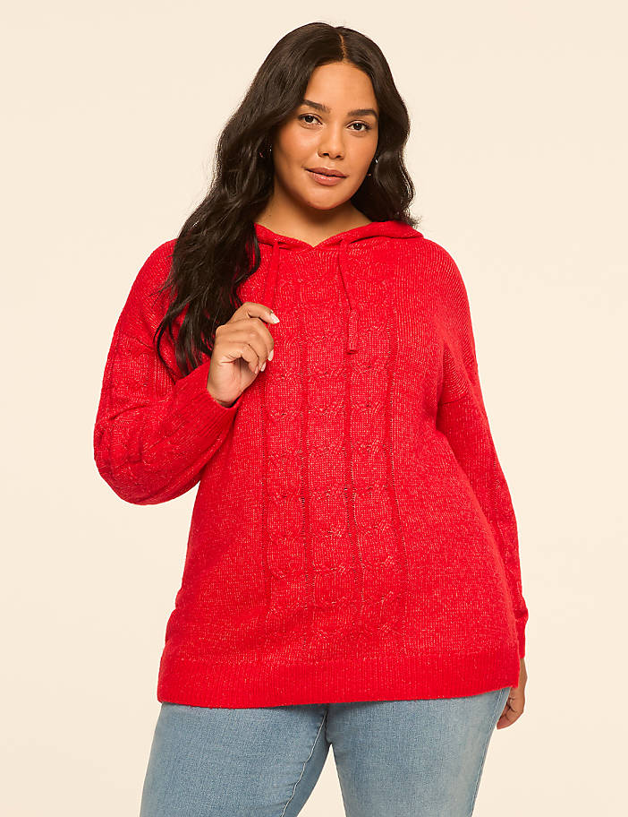 A woman in a red cable-knit hoodie stands against a plain, light-colored background.