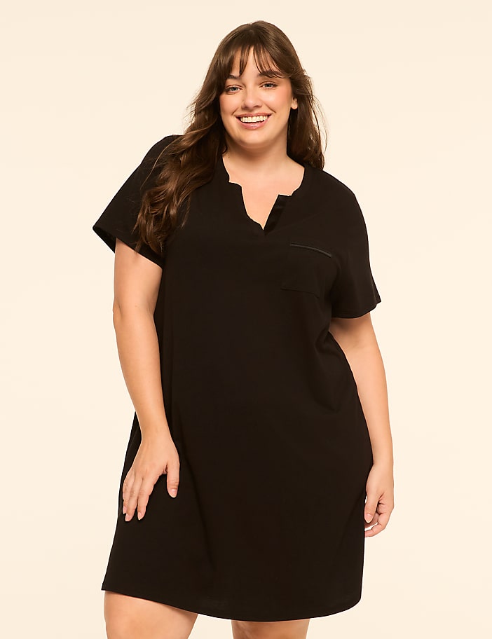A smiling woman in a black dress stands against a plain, light-colored background.