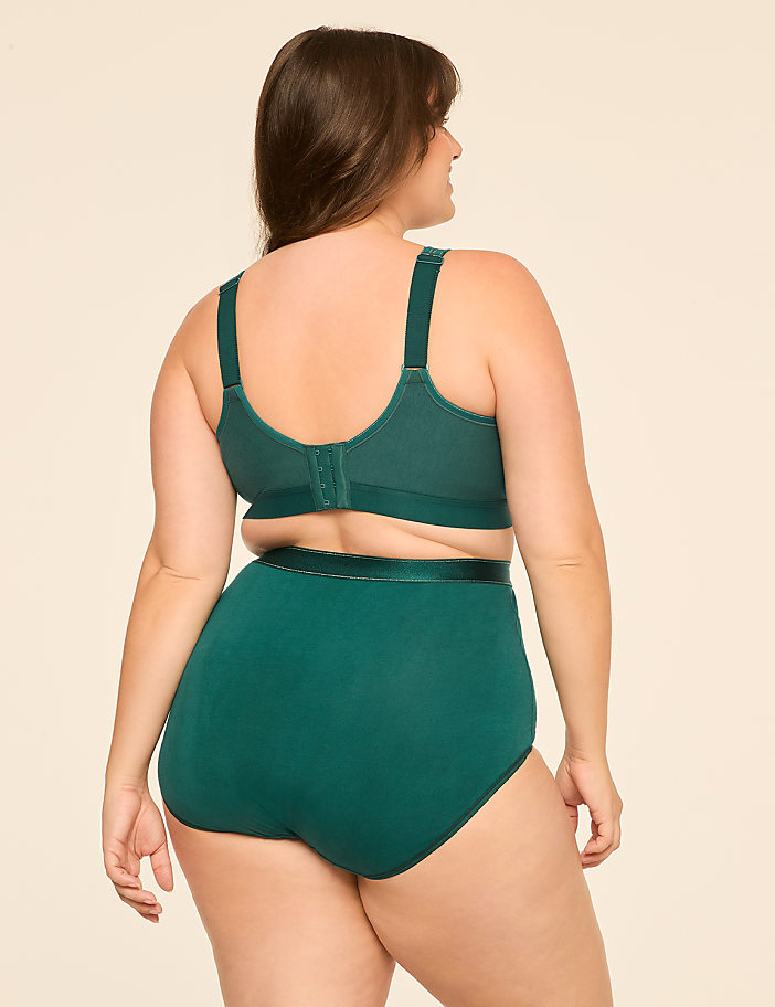 A woman in a green bra and high-waisted underwear stands against a plain, light-colored background.