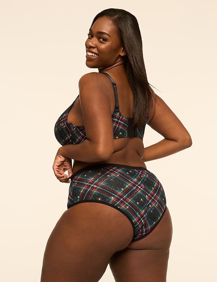 A woman in plaid lingerie smiles over her shoulder against a plain, light-colored background.