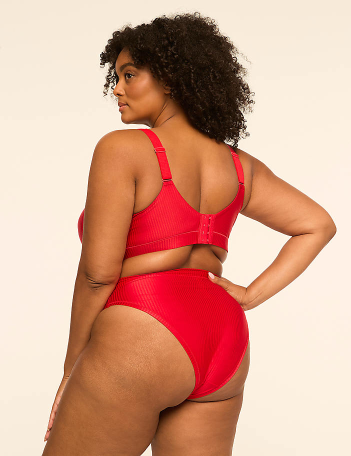 A woman in a red bra and underwear stands against a plain, light-colored background.