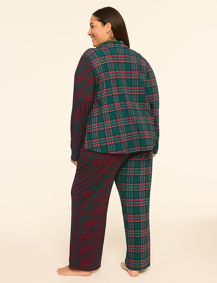 A woman stands in pajamas with a plaid top and patterned pants against a plain, light background.