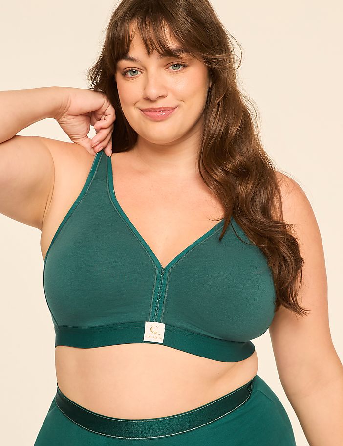 A smiling woman with brown hair and a green bra is posed against a plain, light-colored background.