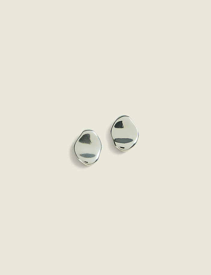 Two silver, pebble-shaped earrings rest on a pale, textured background.