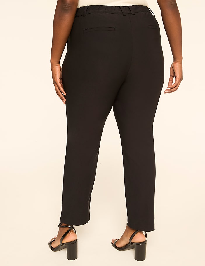 A person wearing black pants and heels stands against a plain, light-colored background.